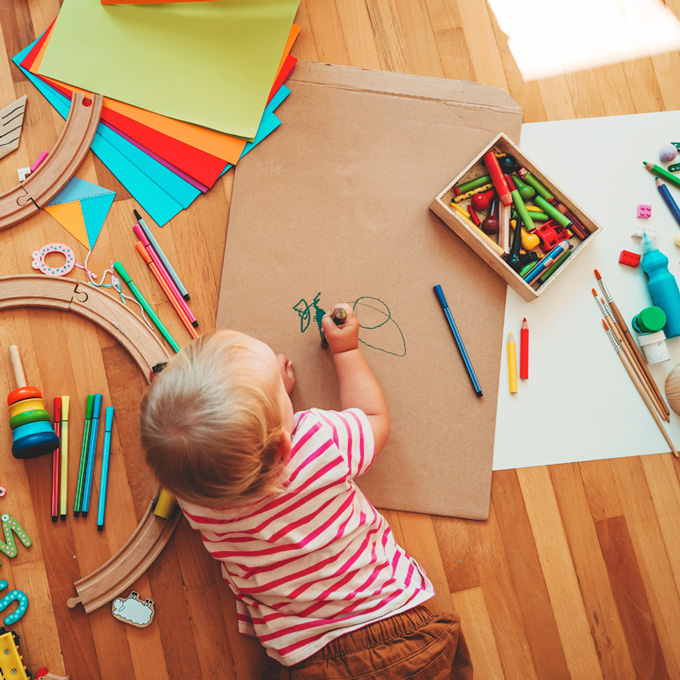 Child is playing on the floor and surrounded by all kinds of toys