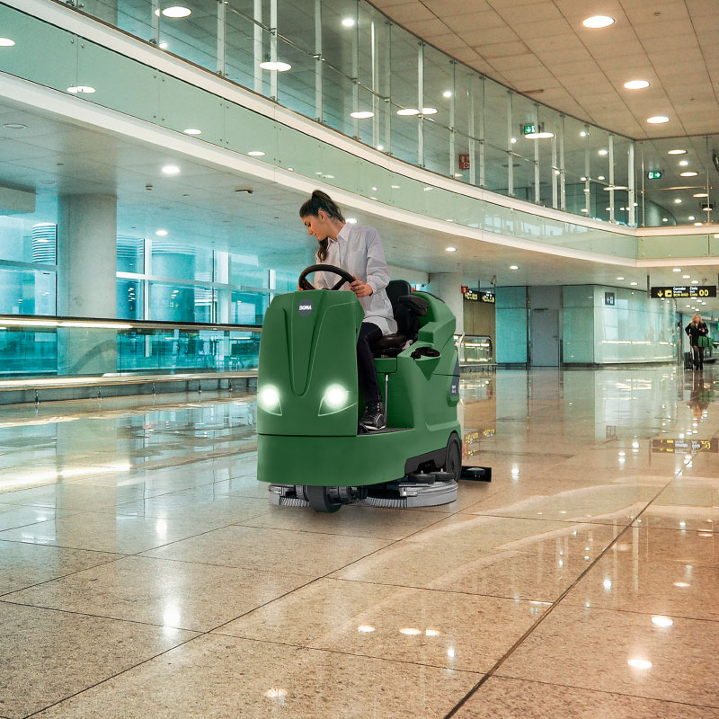 A cleaner sits on a cleaning machine and cleans the hall of an airport.